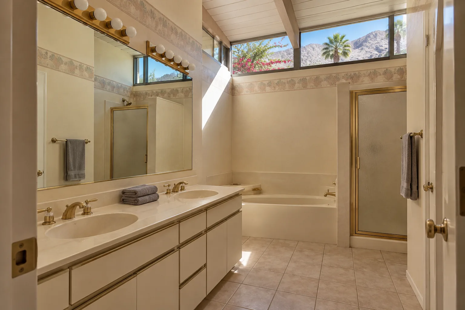 Dated primary bathroom with a white laminate double vanity, cultured marble tops, Hollywood light bars, a drop-in soaking tub and a brass-framed shower door under clerestory windows